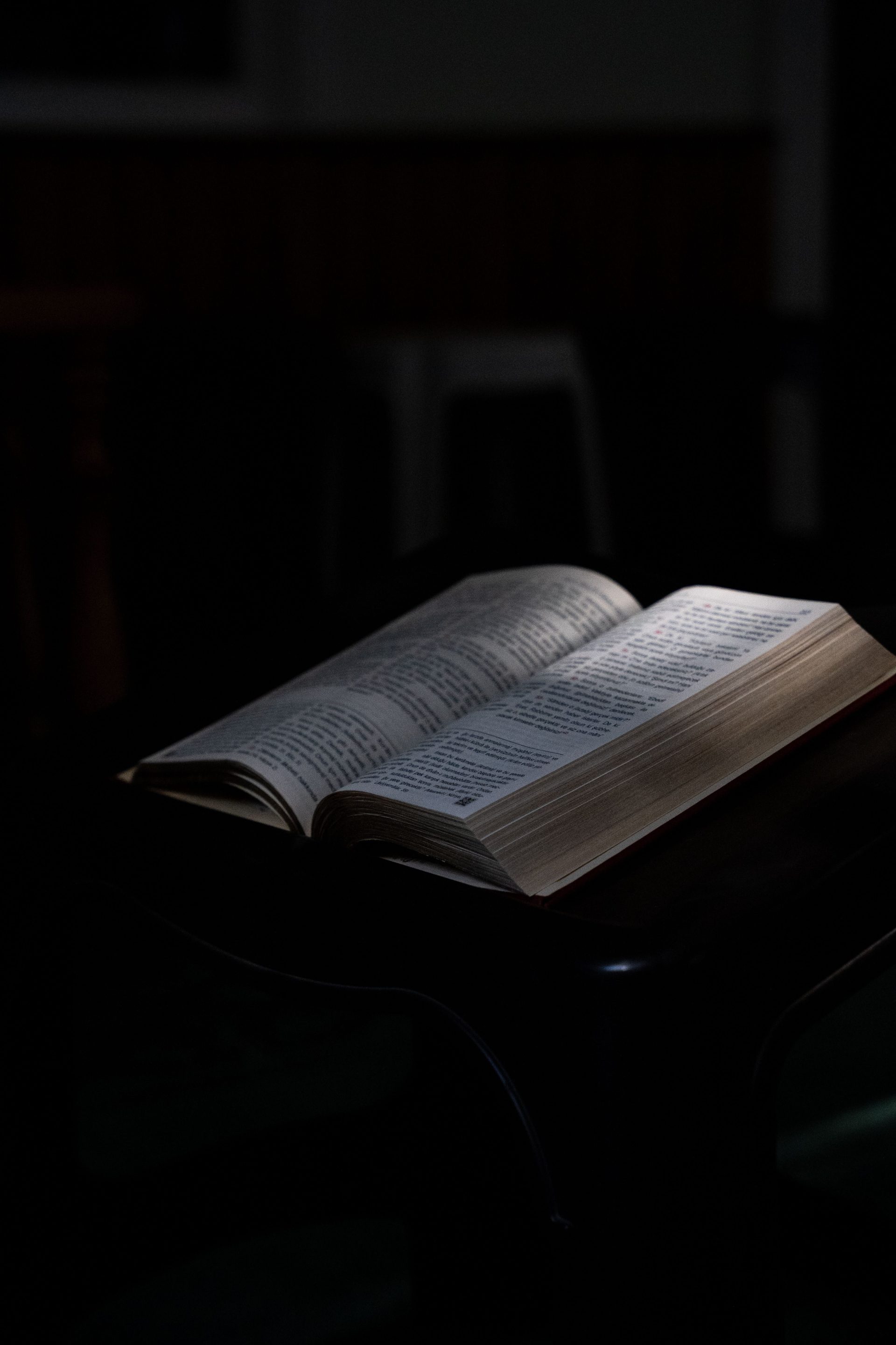 An open book lit by dim light on a dark wooden table, creating a mysterious atmosphere.
